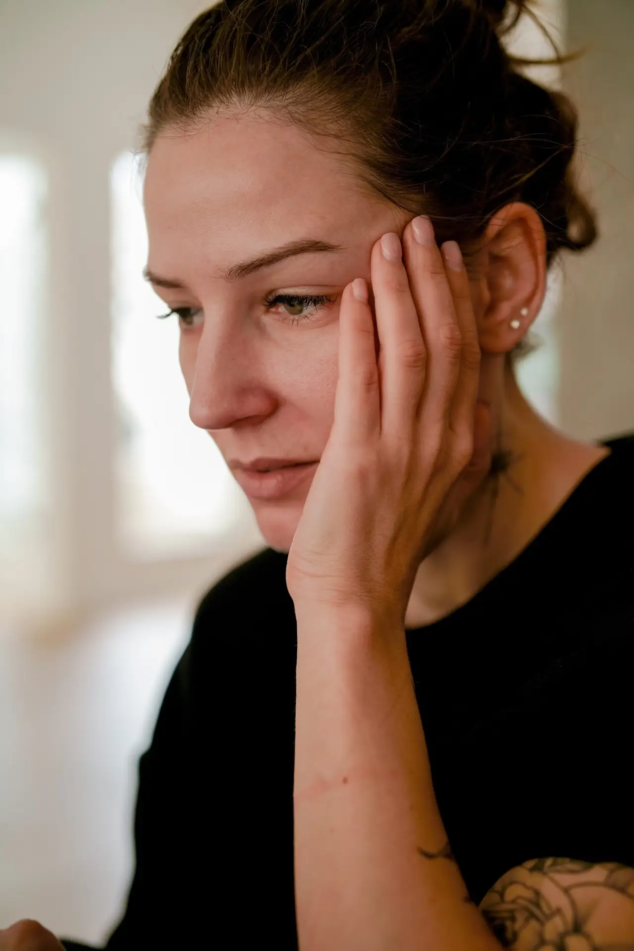 A woman staring at the floor with her hand to her face.