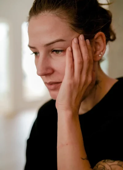 A woman staring at the floor with her hand to her face.