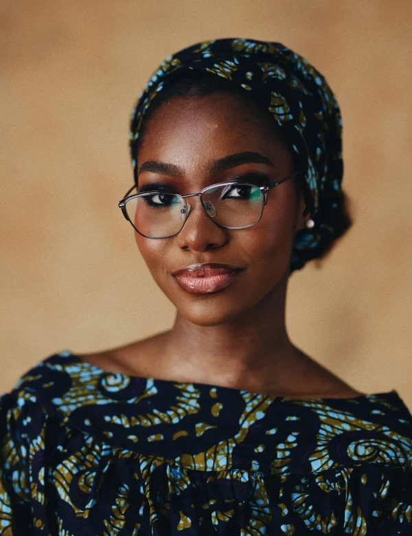 Portrait of a stylish woman wearing glasses and a patterned headscarf with a warm background.